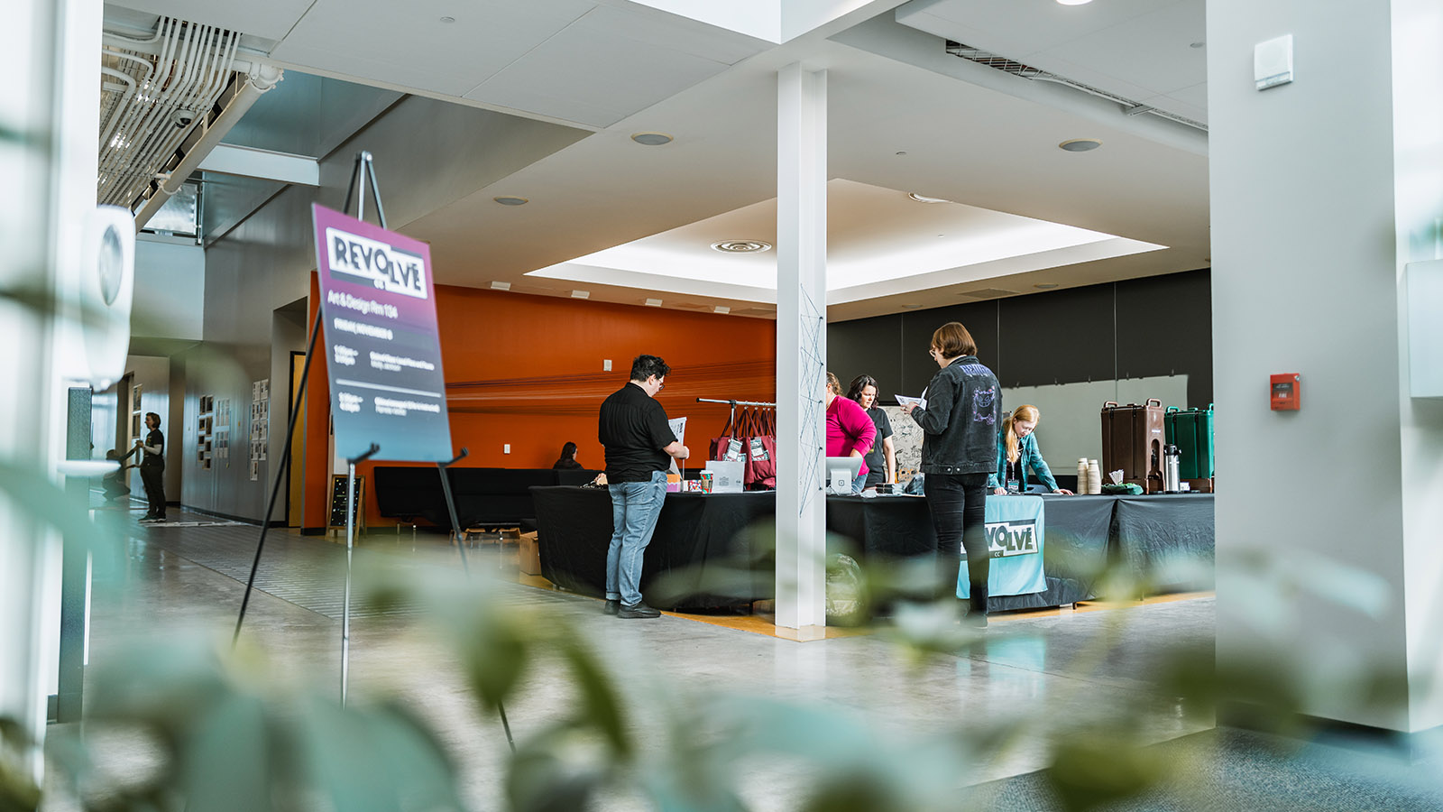 A registration table in an academic building at a college fine arts building. A few people stand around, getting information from volunteers.